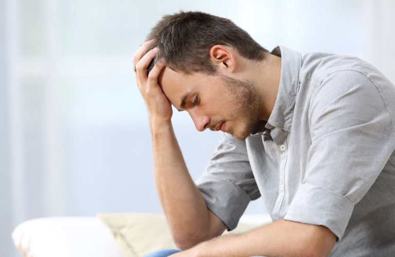 sad man with hand on head sitting on sofa