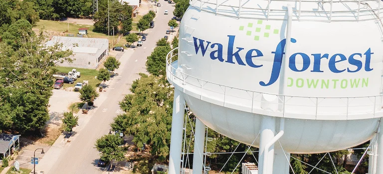 Aerial view of Wake Forest's water tower with "Downtown" branding, surrounded by trees and nearby buildings on a sunny day.