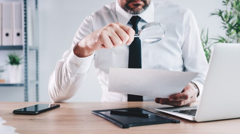 man looks at documents through a magnifying glass